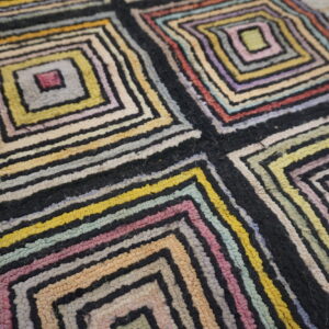 Chunky, multicolored rug with concentric square patterns and thick black separating lines on light wood floor.