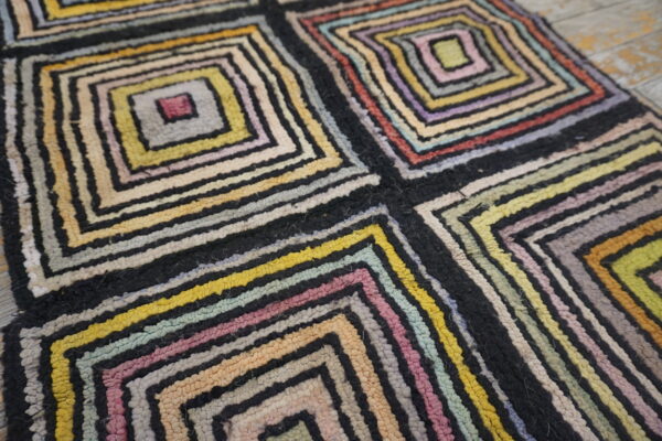 Chunky, multicolored rug with concentric square patterns and thick black separating lines on light wood floor.