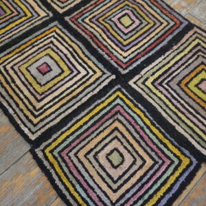 Multicolored high-pile rug featuring large geometric blocks of concentric squares on worn wood planks.