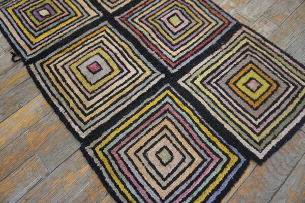 Multicolored high-pile rug featuring large geometric blocks of concentric squares on worn wood planks.