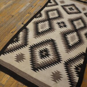 Black, gray, and cream geometric flatweave rug featuring a zig-zag design rests on worn wood planks.