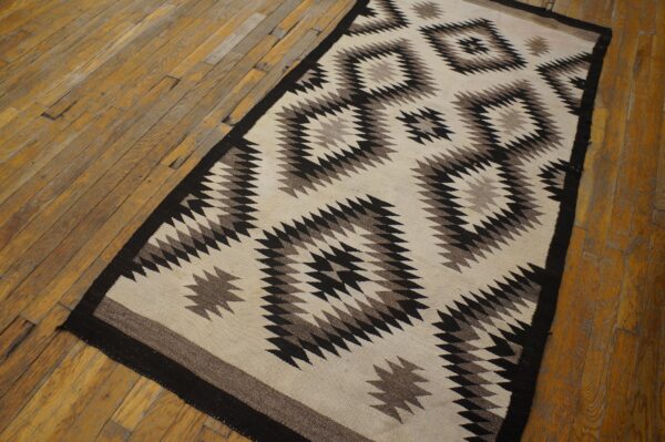 Black, gray, and cream geometric flatweave rug featuring a zig-zag design rests on worn wood planks.