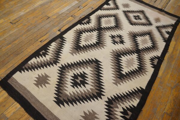 Cream rug runner with large black and brown geometric diamond patterns rests on worn wood planks.