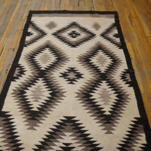 A cream, black, and brown geometric runner rug lies on worn wood plank flooring.
