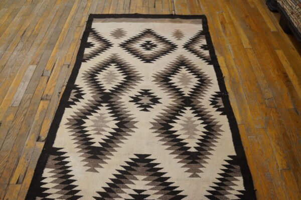A cream, black, and brown geometric runner rug lies on worn wood plank flooring.
