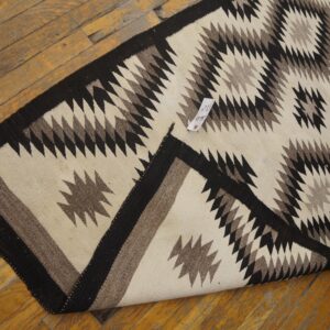 Geometric off-white, brown, and black flatweave rug on worn wood planks, next to a person's foot.