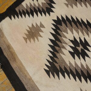 Flatwoven rug in cream, black, and brown features serrated geometric patterns over a distressed wood floor.