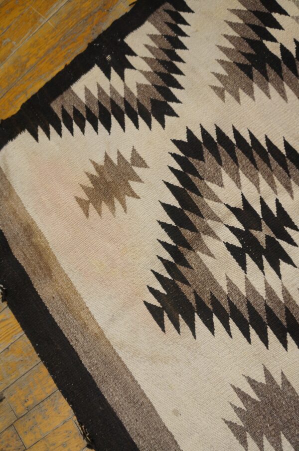 Flatwoven rug in cream, black, and brown features serrated geometric patterns over a distressed wood floor.
