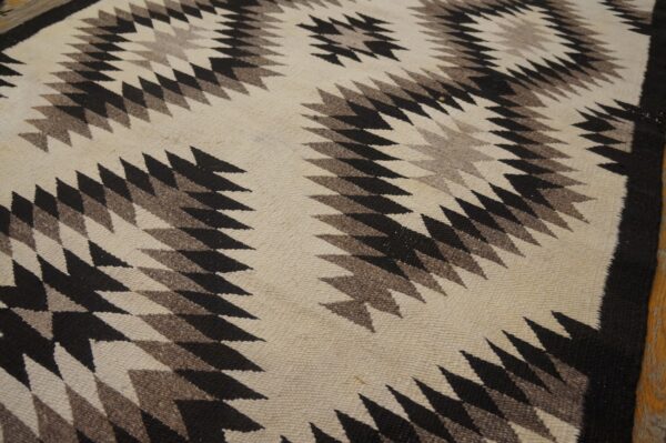 Flatweave rug with serrated zigzag patterns in cream, black, and medium brown on a wood floor.