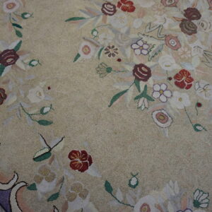 A close-up shows a beige textured floral rug with a purple border lying on light wood planks.
