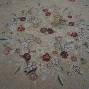 Close-up of a beige textured rug with a central bouquet of red, purple, pink, and green stylized flowers.