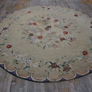 Round tan rug with dense floral patterns and a scalloped purple border resting on aged wooden floorboards.