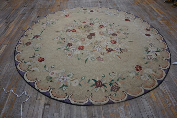 Round tan rug with dense floral patterns and a scalloped purple border resting on aged wooden floorboards.