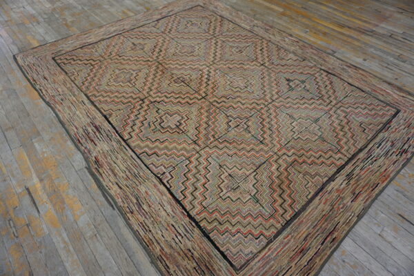 A low-pile rug with concentric zigzag squares and a wide rag-style border rests on distressed wood flooring.