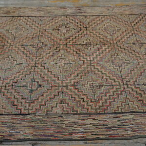 A textured rug with a repeating geometric zigzag pattern is displayed on rustic gray wood plank flooring.