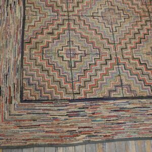 Multicolored geometric rug with a zigzag pattern and thick striped border on rustic wooden floorboards.