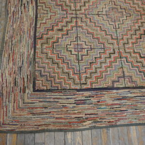 Highly textured, multicolored rug featuring a stepped diamond pattern rests on distressed wood flooring.