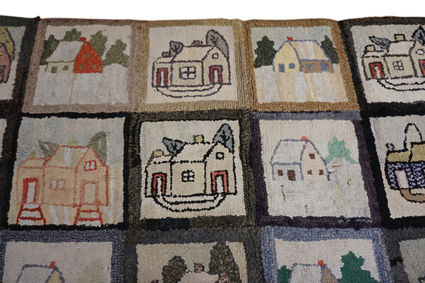 Colorful square rug patches showing naive house designs displayed on distressed wood flooring with rolled rugs nearby.