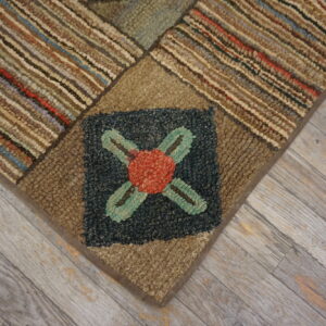 Close-up of a chunky patchwork rug featuring brown stripes and a dark blue square with a red floral motif, on gray wood floor.