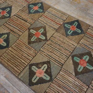 Earth-toned, textured hooked runner rug with floral patches and striped blocks rests on distressed gray plank flooring.