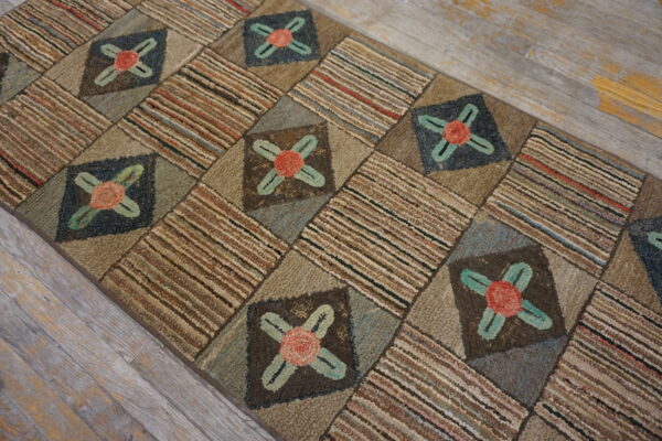 Earth-toned, textured hooked runner rug with floral patches and striped blocks rests on distressed gray plank flooring.