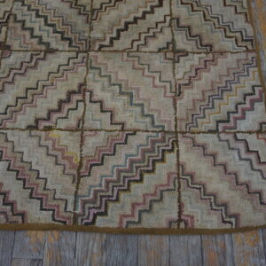 High-pile rug with geometric zig-zag pattern in muted pink, black, and blue on worn wooden flooring.