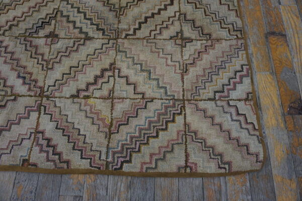 High-pile rug with geometric zig-zag pattern in muted pink, black, and blue on worn wooden flooring.