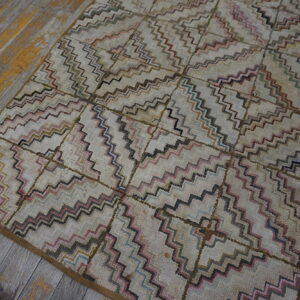 Geometric rug with pink, teal, and brown zigzag lines on a cream field, placed on distressed wood floors.