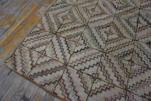 Geometric rug with pink, teal, and brown zigzag lines on a cream field, placed on distressed wood floors.
