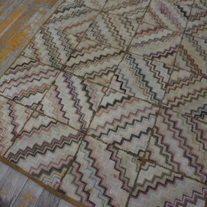 Geometric cream rug featuring multi-colored zigzags and squares lies on weathered wood floorboards.