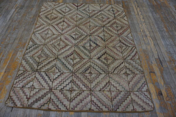 A textured rug with multicolored zig-zag diamonds on a light background rests on worn gray wood flooring.