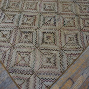 A muted geometric rug featuring zigzag lines within squares lies on distressed gray and brown wooden floors.
