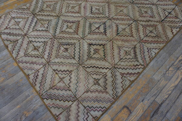 A muted geometric rug featuring zigzag lines within squares lies on distressed gray and brown wooden floors.