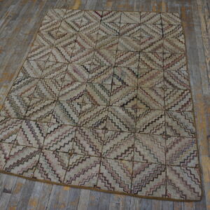 Muted rug with a multicolored zigzag diamond pattern displayed on distressed gray wooden flooring.