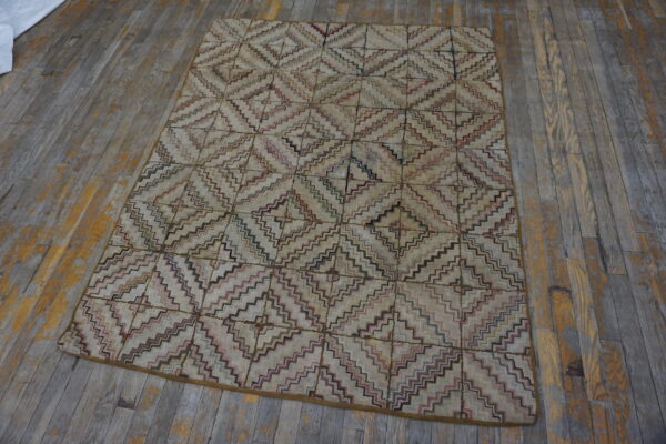 Muted rug with a multicolored zigzag diamond pattern displayed on distressed gray wooden flooring.