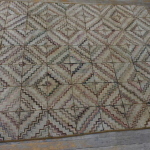 Low-pile rug with repeating multicolored zigzag diamond pattern rests on distressed gray plank flooring.