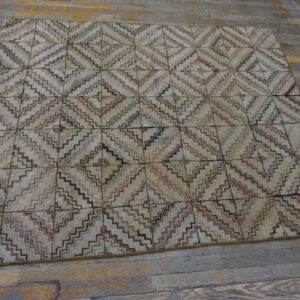 A multi-color, stepped diamond rug with a beige field rests on distressed gray wood plank flooring.