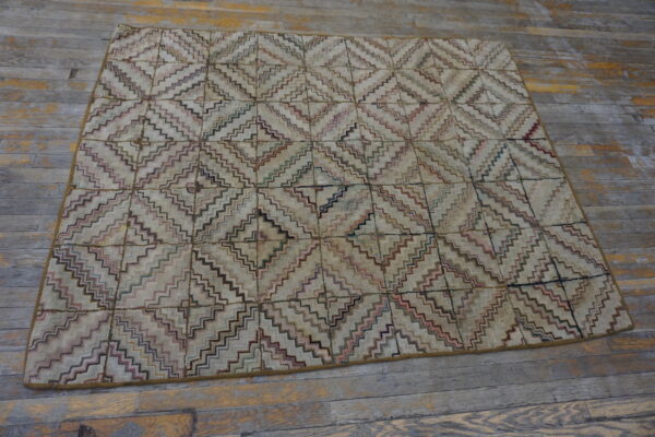 A multi-color, stepped diamond rug with a beige field rests on distressed gray wood plank flooring.