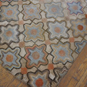 A high-texture rug with blue and orange quatrefoil motifs lies on warm, distressed wood flooring.
