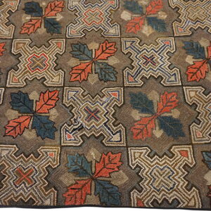 Hooked rug with alternating square motifs of coral and teal leaves and elaborate geometric shapes.