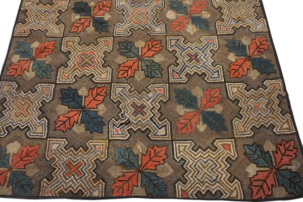 Hooked rug with alternating square motifs of coral and teal leaves and elaborate geometric shapes.