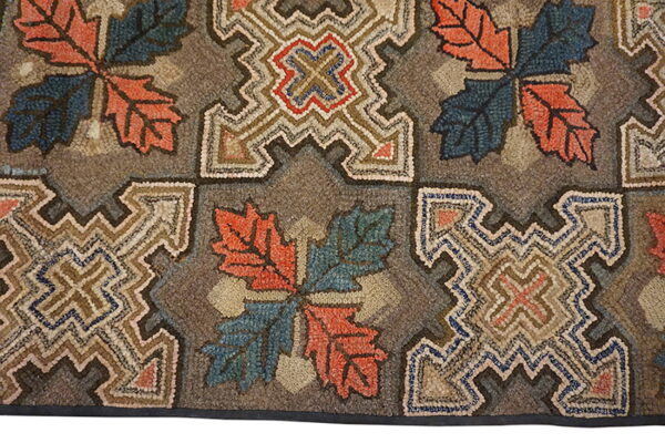 Coarse, hooked rug featuring rustic orange and blue leaf motifs alternating with complex tan geometric blocks.