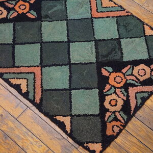 Textured rug with sage and dark green squares, black borders, and peach florals lies on distressed hardwood floor.