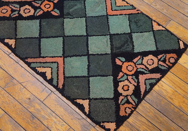 Textured rug with sage and dark green squares, black borders, and peach florals lies on distressed hardwood floor.