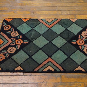 A dark green, black, and orange rug featuring a diamond center and stylized floral corners rests on wood planks.