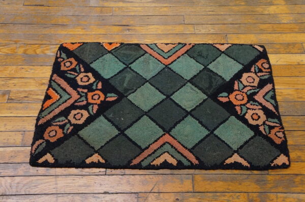 A dark green, black, and orange rug featuring a diamond center and stylized floral corners rests on wood planks.