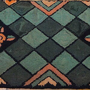 A hooked rug featuring dark green diamonds and orange floral motifs on a black border over wood flooring.