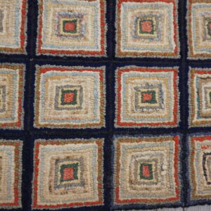 Multicolored hooked rug featuring chunky, concentric log cabin squares separated by a navy blue grid.