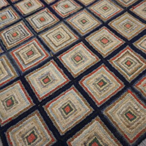 Textured navy rug with a repeating multi-colored log cabin style diamond pattern resting on whitewashed wood planks.