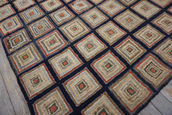 Textured navy rug with a repeating multi-colored log cabin style diamond pattern resting on whitewashed wood planks.